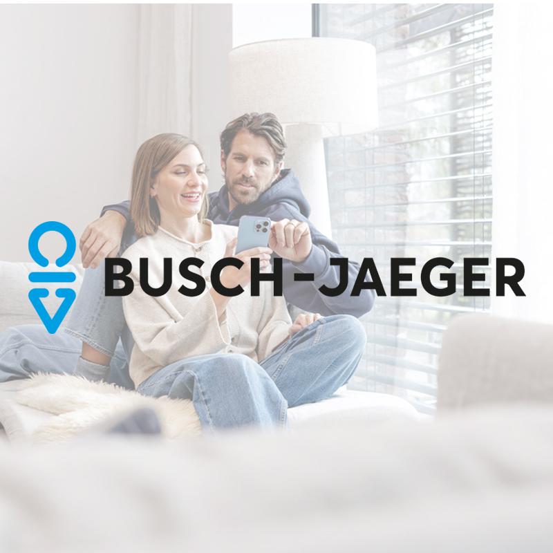 Ein Paar sitzt entspannt auf einem Sofa und bedient gemeinsam ein Smartphone. Mittig im Bild steht das Busch-Jaeger Logo auf hellem, minimalistischem Hintergrund.