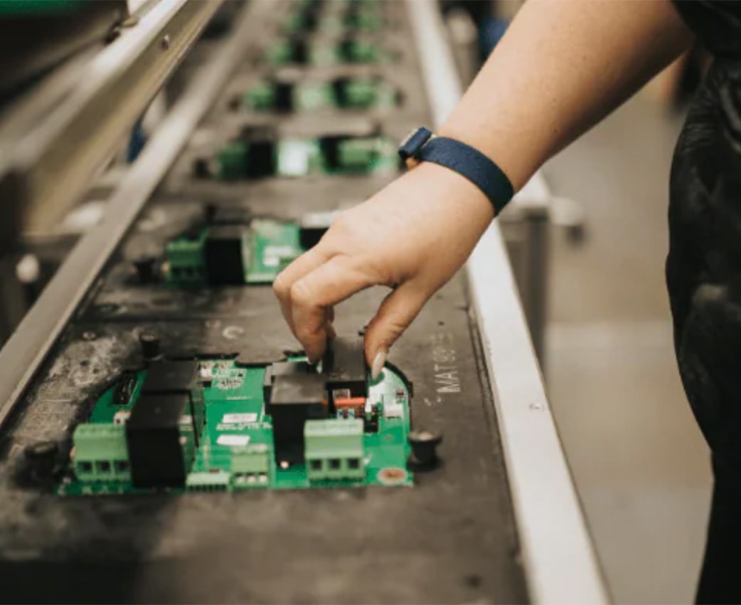 Elektronik der zappi Wallbox auf einem Produktionsband mit Hand eines mitarbeitenden Menschen