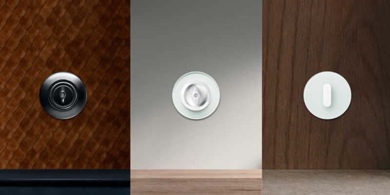 Vergleich dreier runder Hager Design-Lichtschalter: Links ein schwarzer Drehknebel-Schalter auf braunem Rauten-Leder, mittig ein runder Glasschalter auf neutralem Grund und rechts ein weißer Kippschalter auf dunkler Holzvertäfelung.