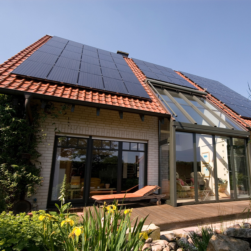 Außenansicht eines Einfamilienhauses mit einer großflächigen PV-Anlage auf dem Dach und einem modernen Glas-Anbau.