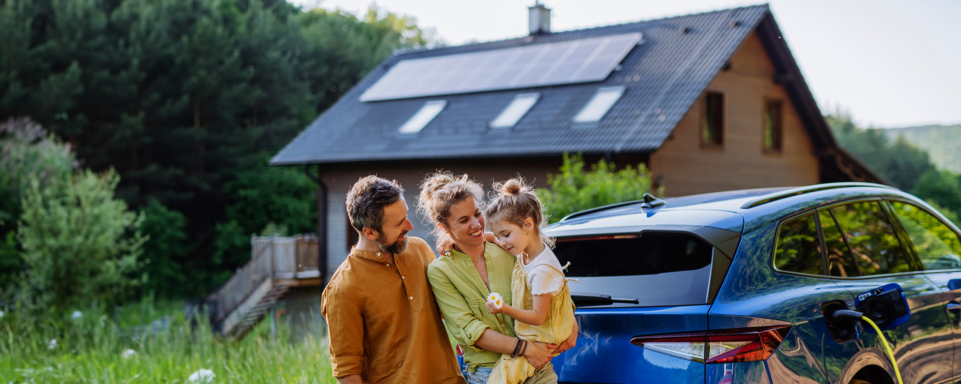 Glueckliche Familie mit Elektroauto und Haus mit Solaranlage