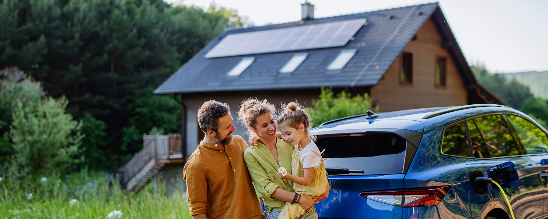 Hero Shot KfW-Foerderung 442 Solarstrom fuer Elektroautos Glueckliche Familie mit Elektroauto und Haus mit Solaranlage