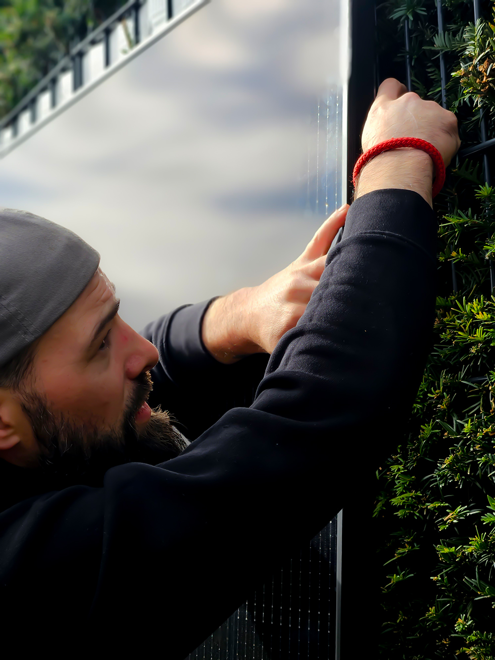 Nahaufnahme von einem Mann mit umgedrehten Basecap, befestigt PV-Modul am Zaun